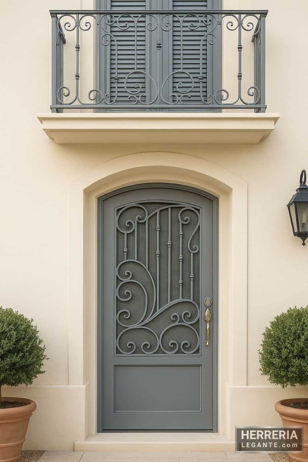Puerta de herrería gris con diseño curvo, junto a balcón de hierro forjado en fachada estilo mediterráneo