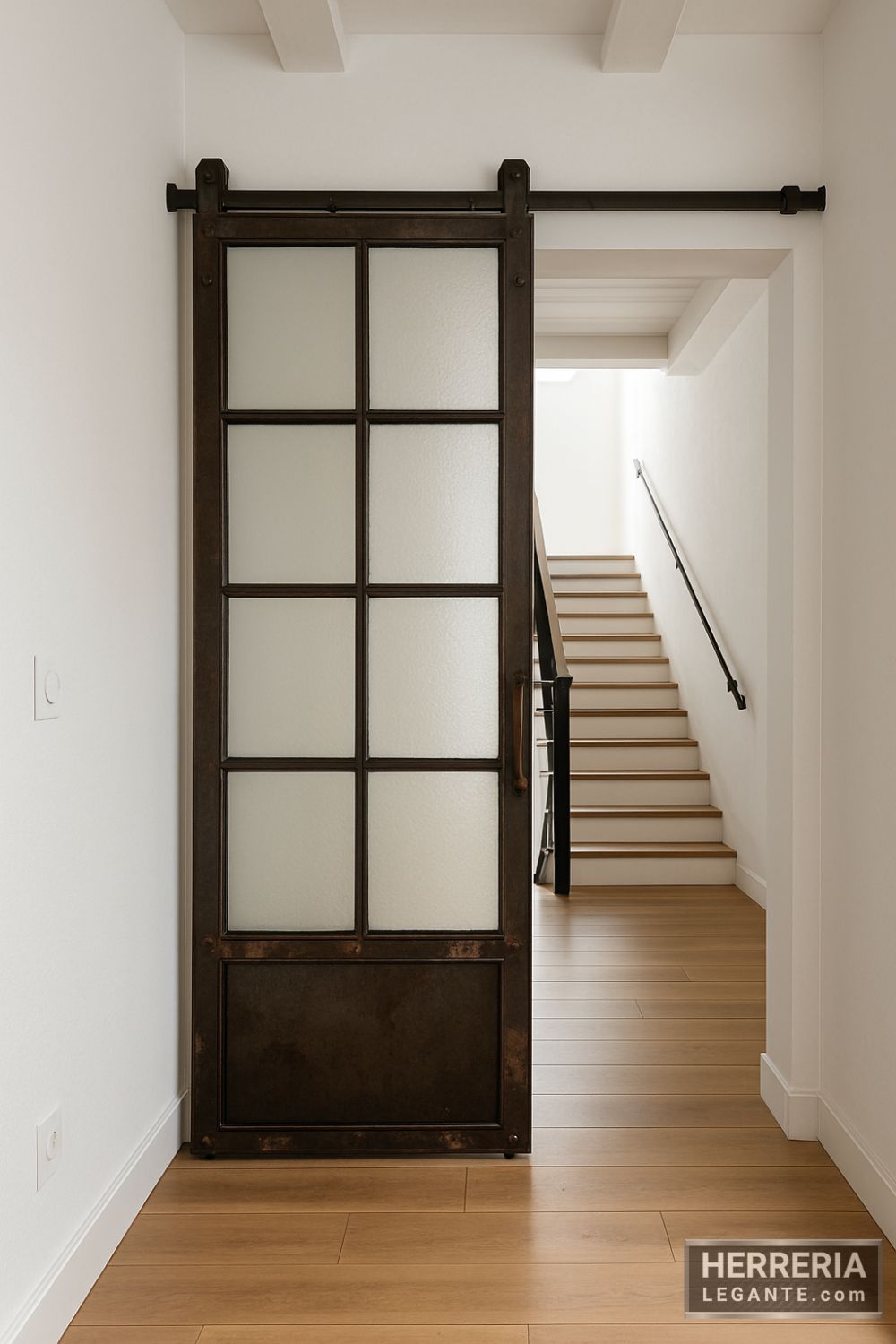 Puerta corrediza industrial de hierro envejecido con vidrio segmentado, instalada entre pasillo y escalera en vivienda tipo dúplex