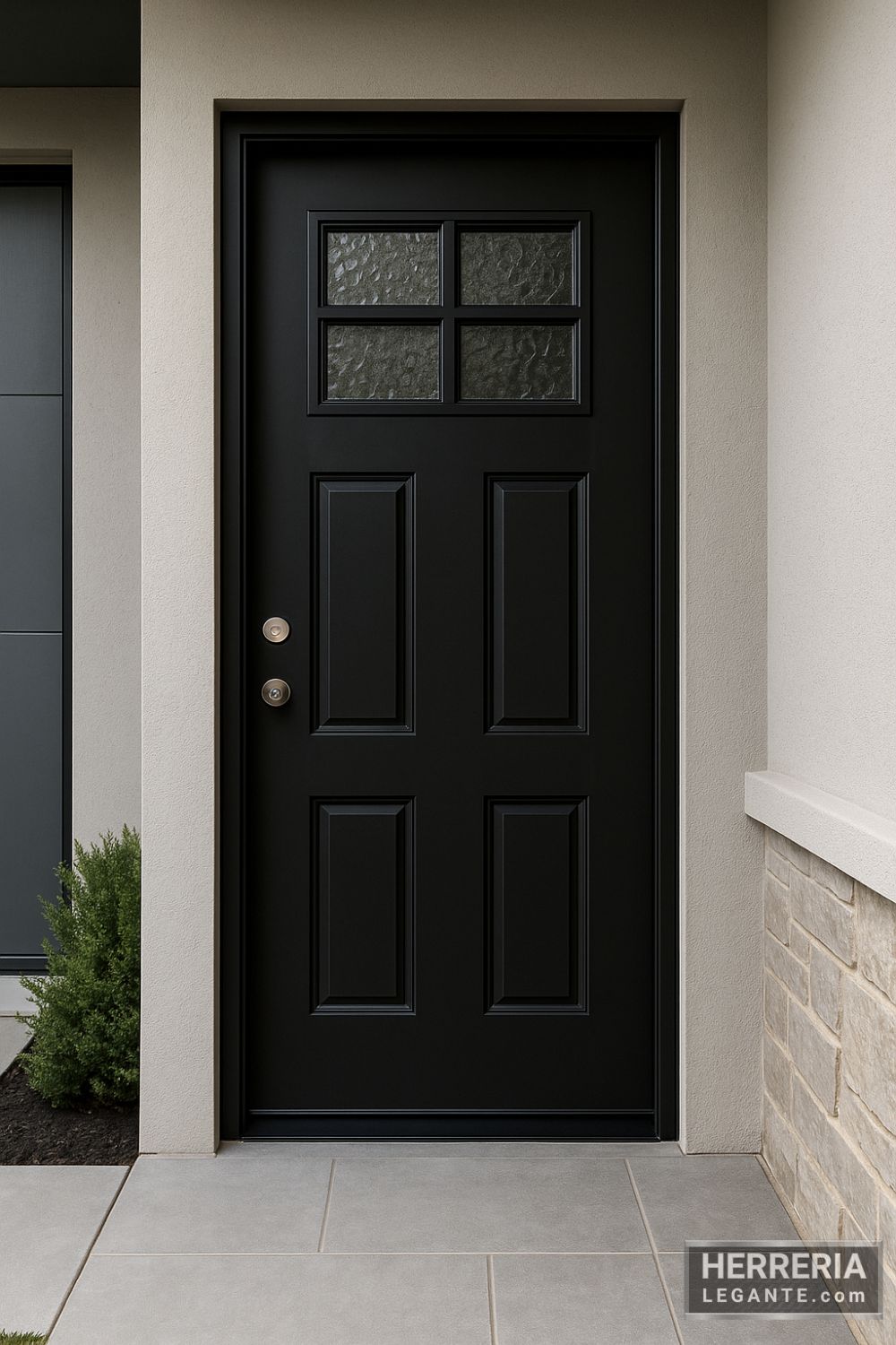 Puerta de herrería moderna en acabado negro mate con ventanales superiores de vidrio texturizado, instalada en fachada minimalista con muros claros y piso gris