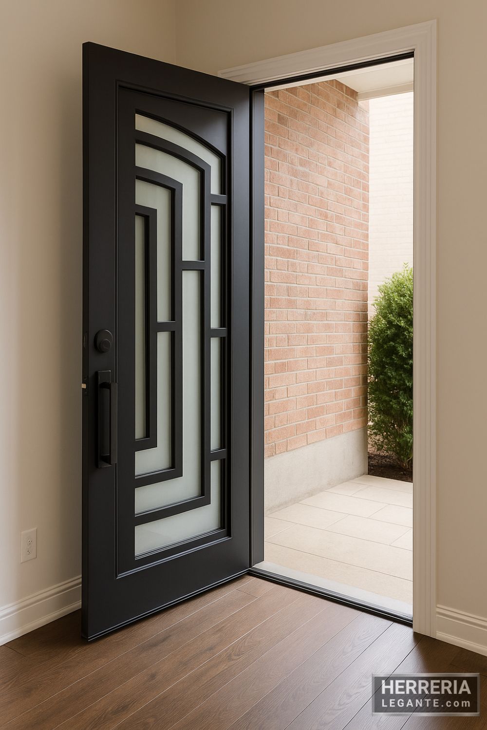 Puerta de herrería negra con diseño geométrico y vidrio esmerilado, abierta hacia el exterior con pared de ladrillo y arbusto