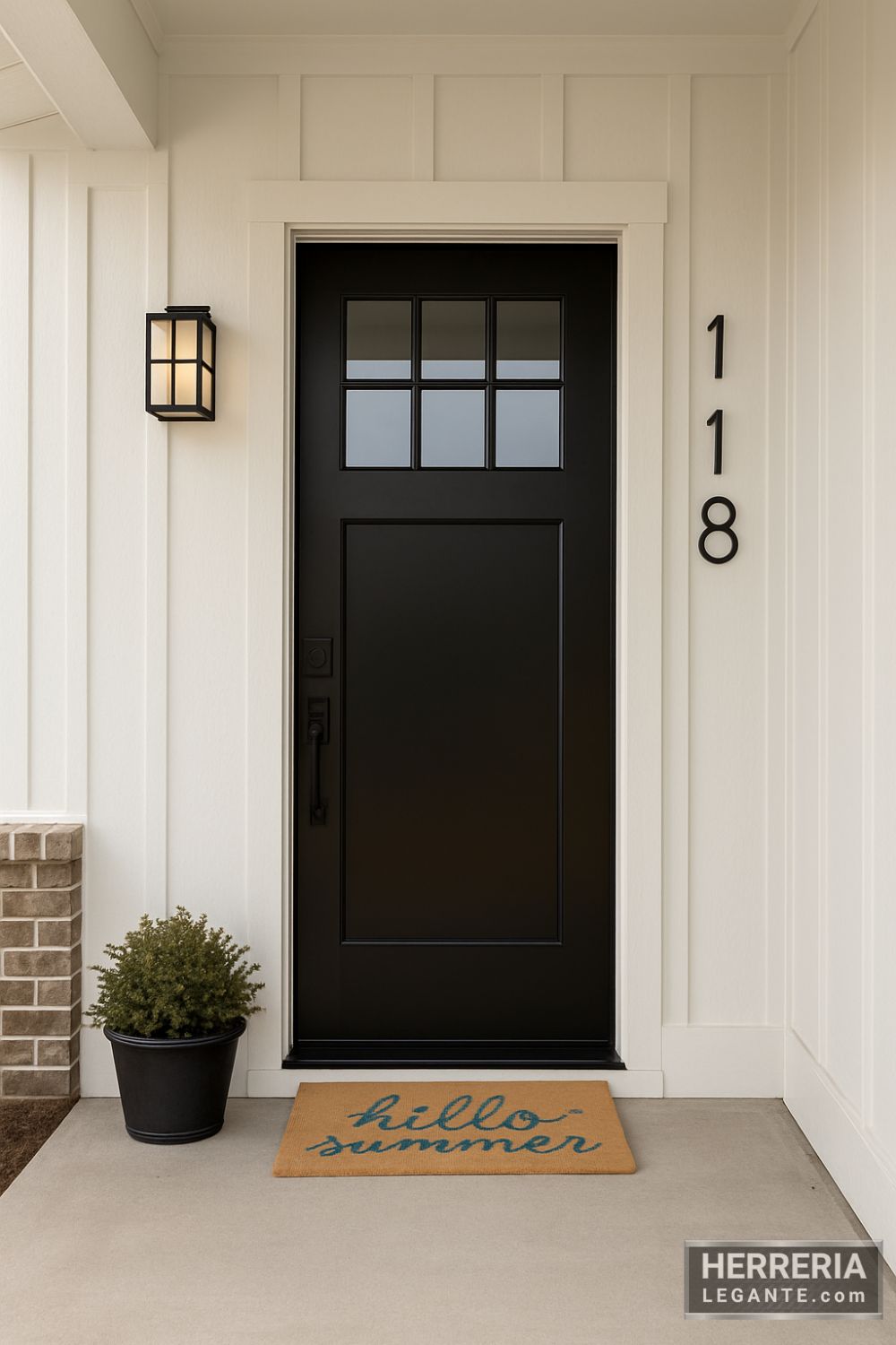 puerta de herrería negra con tragaluz dividido en seis secciones y panel inferior liso, instalada en entrada principal de casa moderna con fachada clara